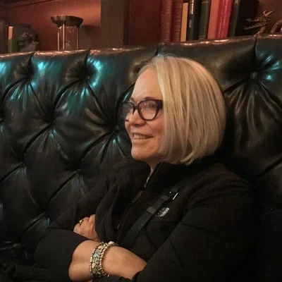 A woman with glasses sitting on a dark green leather couch, smiling.